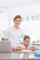 Little girl doing her homework with mother using laptop