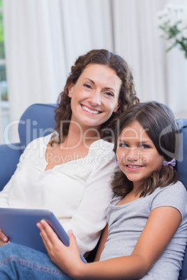 Happy mother and daughter sitting on the couch and using tablet