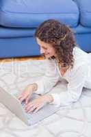 Smiling woman lying on the floor and using her laptop