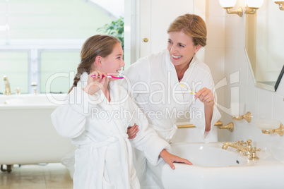 Happy mother and daughter brushing teeth together