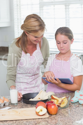 Happy mother and daughter preparing cake together with tablet