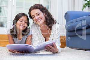 Happy mother and daughter lying on the floor and reading a book