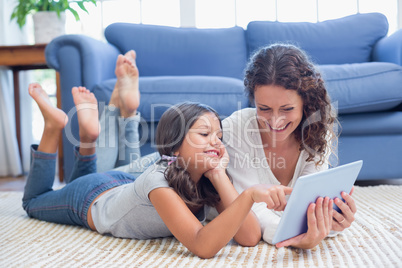 Happy mother and daughter lying on the floor and using tablet