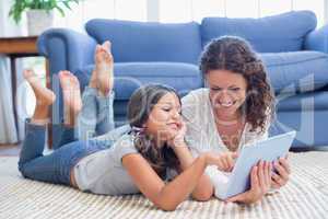 Happy mother and daughter lying on the floor and using tablet