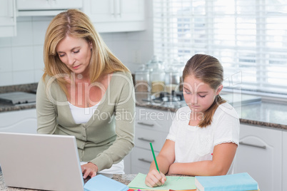 Mother using laptop while daughter doing homework