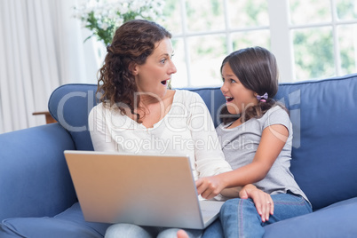 Happy mother and daughter sitting on the couch and using laptop