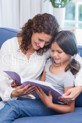 Happy mother and daughter sitting on the couch and reading book