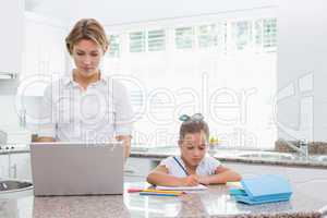 Little girl doing her homework with mother using laptop