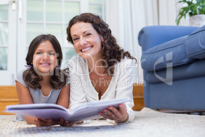 Happy mother and daughter lying on the floor and reading a book