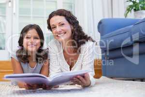 Happy mother and daughter lying on the floor and reading a book