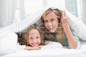 Mother and daughter looking at camera under the duvet