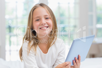 Little girl using tablet pc sitting on her bed