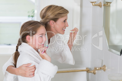 Happy mother and daughter brushing teeth together