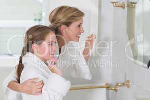 Happy mother and daughter brushing teeth together