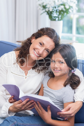 Happy mother and daughter sitting on the couch and reading book