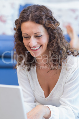 Smiling woman lying on the floor and using her laptop
