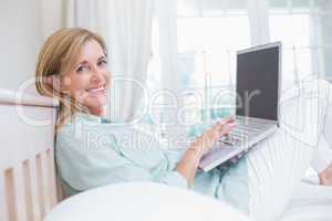 Happy woman using laptop in her bed