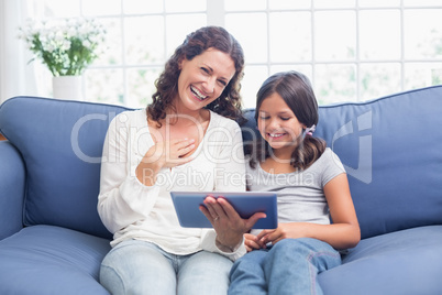 Happy mother and daughter sitting on the couch and using tablet