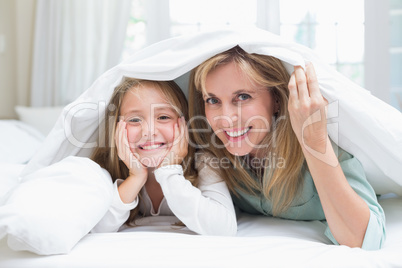 Mother and daughter looking at camera under the duvet