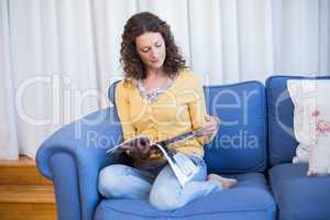 Pretty brunette relaxing on the couch and reading magazine