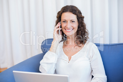 Pretty brunette speaking on the phone while using her laptop