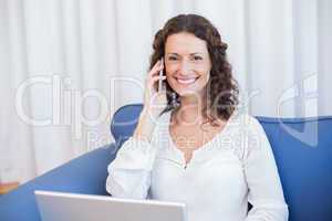 Pretty brunette speaking on the phone while using her laptop