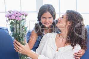 Happy mother and daughter sitting on the couch with flowers