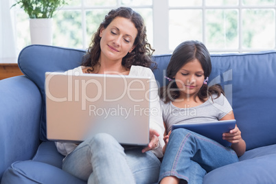 Happy mother and daughter sitting on the couch while using lapto