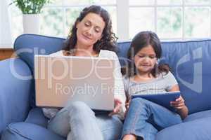 Happy mother and daughter sitting on the couch while using lapto