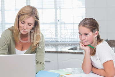 Mother using laptop while daughter doing homework