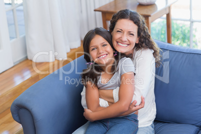 Happy mother and daughter sitting on the couch and smiling at ca
