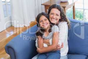 Happy mother and daughter sitting on the couch and smiling at ca