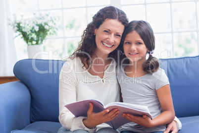 Happy mother and daughter sitting on the couch and reading book