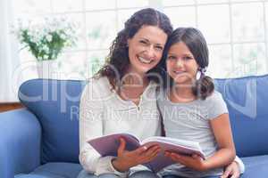 Happy mother and daughter sitting on the couch and reading book