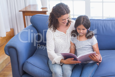 Happy mother and daughter sitting on the couch and reading book