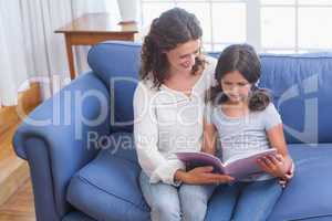 Happy mother and daughter sitting on the couch and reading book