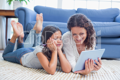 Happy mother and daughter lying on the floor and using tablet