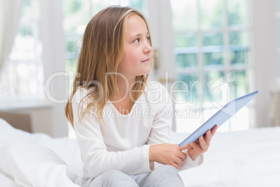 Little girl using tablet pc sitting on her bed