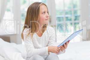 Little girl using tablet pc sitting on her bed