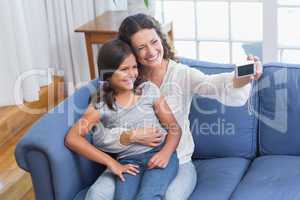 Happy mother and daughter sitting on the couch and taking selfie