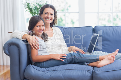 Happy mother and daughter sitting on the couch and using laptop