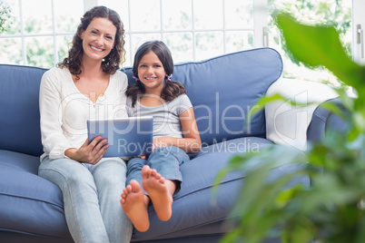 Happy mother and daughter sitting on the couch and using tablet