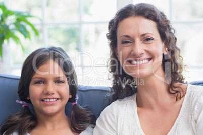 Happy mother and daughter sitting on the couch and smiling at ca