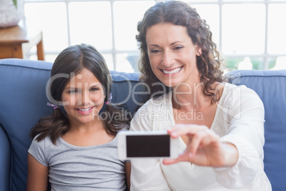 Happy mother and daughter sitting on the couch and taking selfie