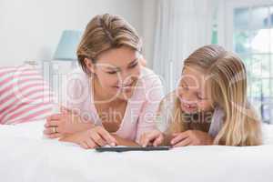 Mother and daughter using tablet together on bed