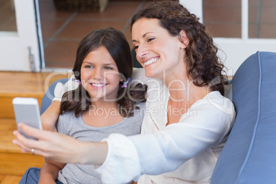 Happy mother and daughter sitting on the couch and taking selfie