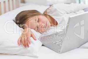 Little girl sleeping in her bed in front of the laptop