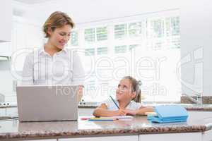 Little girl doing her homework with mother using laptop