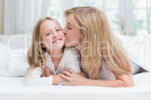 Mother kissing her daughter on the cheek in the bed