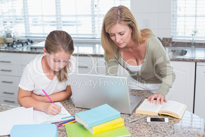 Mother using laptop while daughter doing homework